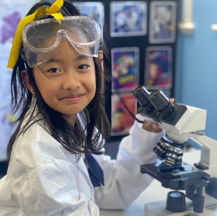 Image of a student seated at a microscope, facing the camera, smiling