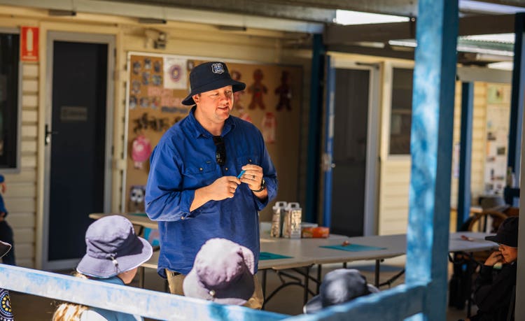 Photo of a teacher addressing students seated outdoors