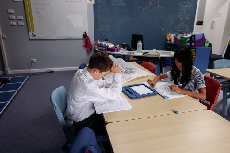 Image of two students seated at a desk with books and ipad in front of them