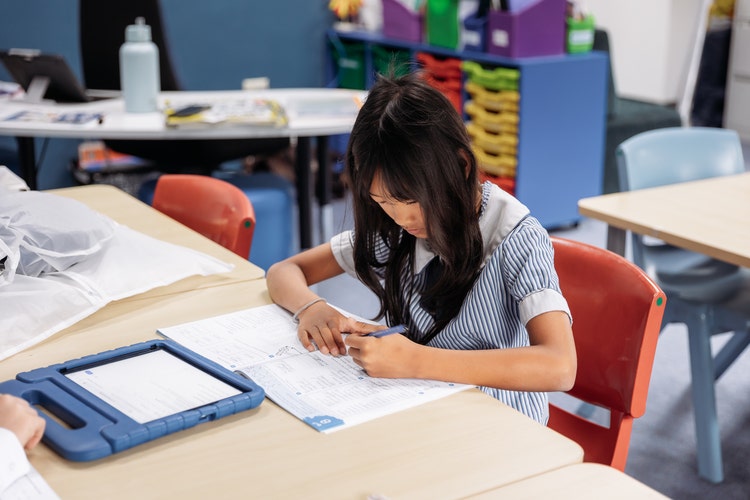 Image of a student, head down, writing at a desk
