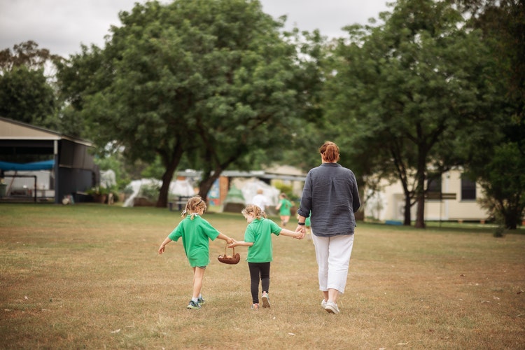 Photo of a teacher and two students, holding hands, with backs to the camera