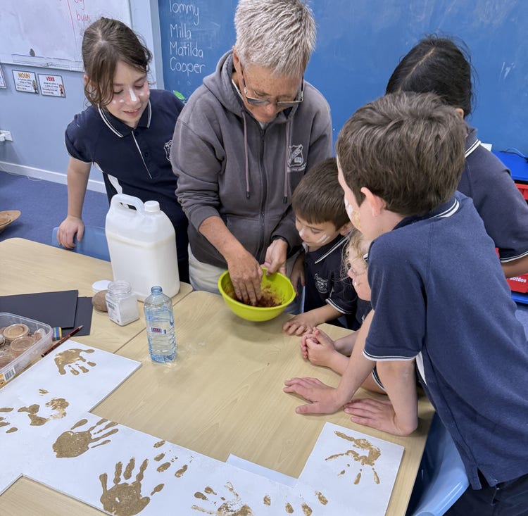 Image of four students crowded around an adult who is holding a bowl, making ochre